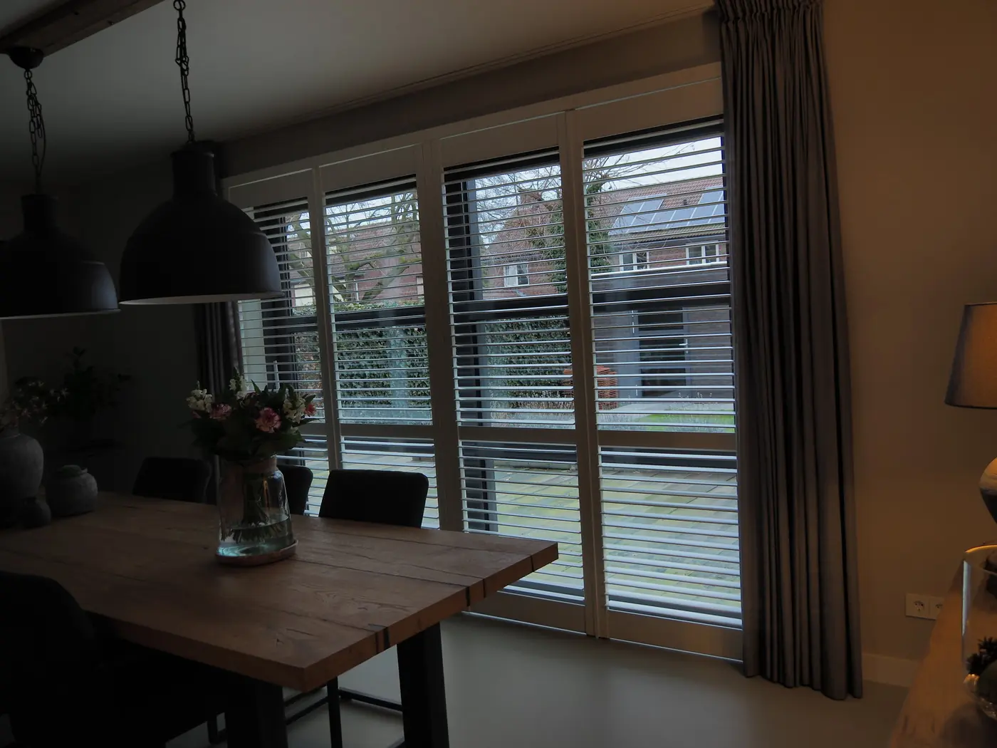 Jaloezieën in een eethoek met eiken tafel en zwarte hanglampen