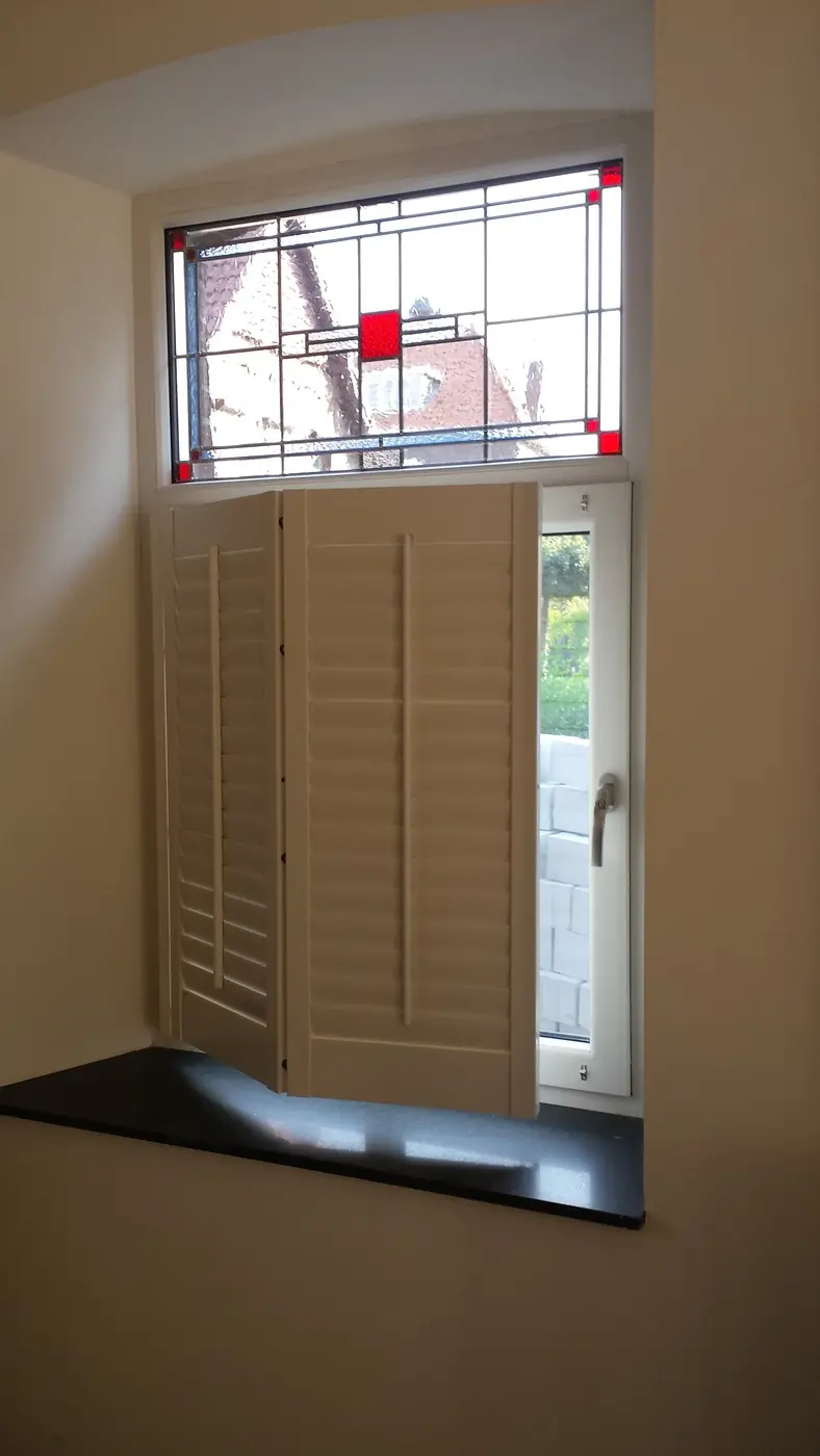 Shutters onder een schuin dakvlak, naast een glas-in-loodraam