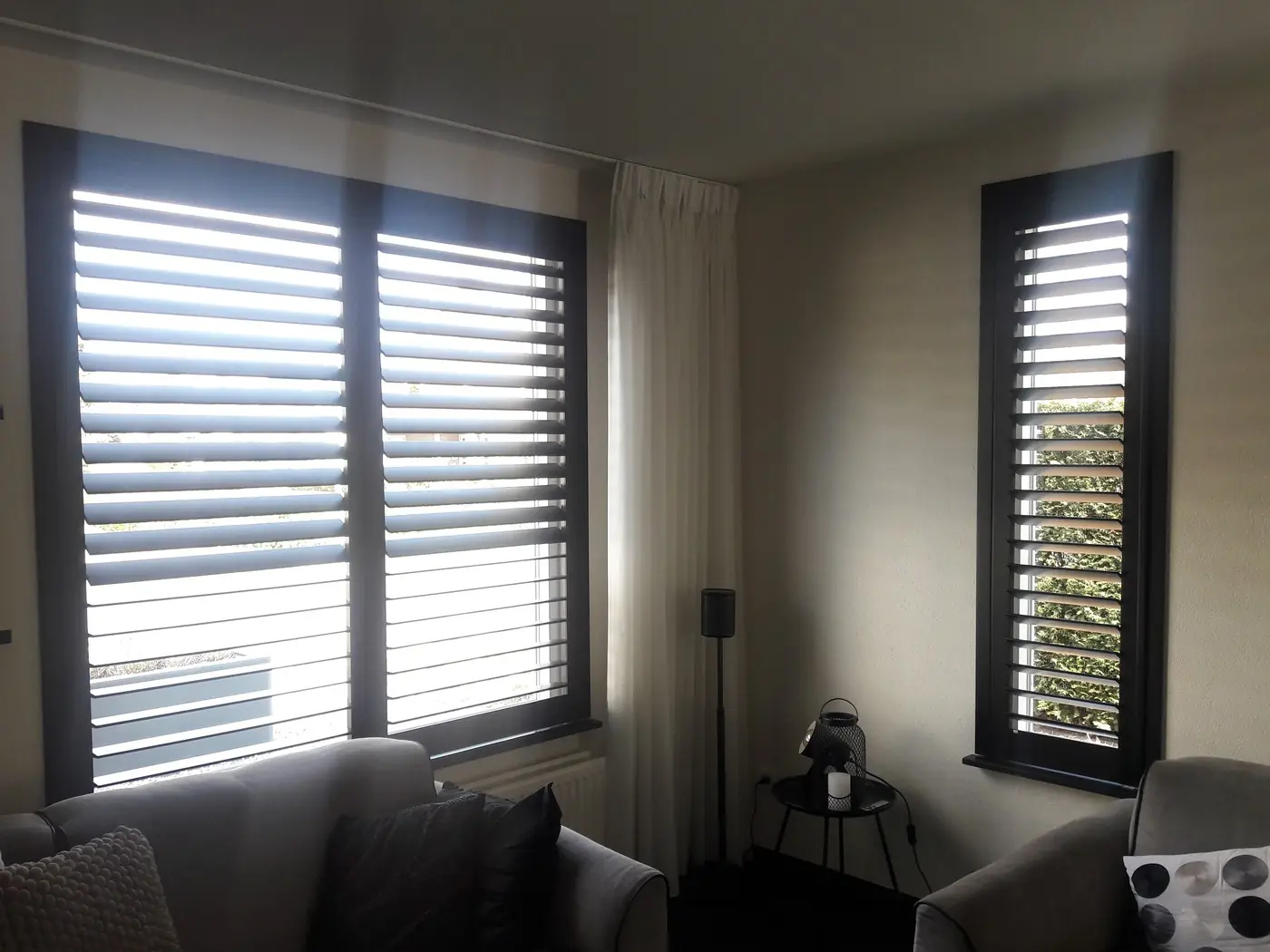 Witte shutters en vitrage in een woonkamer, lamellen half geopend